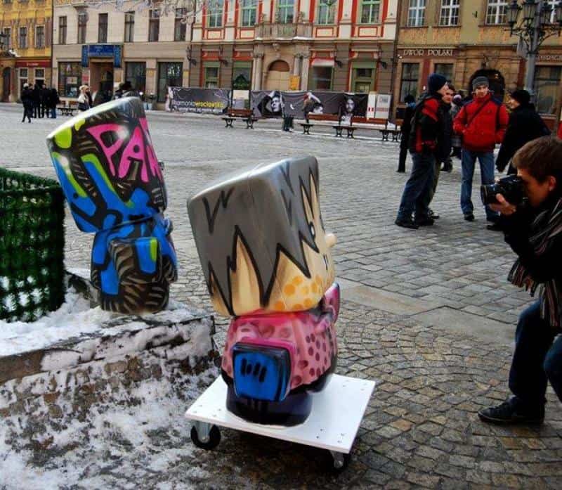 oryg_064490685_1129949550544944_1465385417682452480_o Rzeźby w kształcie postaci w stylu graffiti na rynku miejskim, fotograf robi zdjęcia.