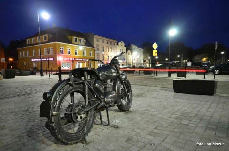 Kultowy Motocykl - Pomnik w Żaganiu 4 Motocykl na placu miejskim nocą, w tle oświetlone kamienice.