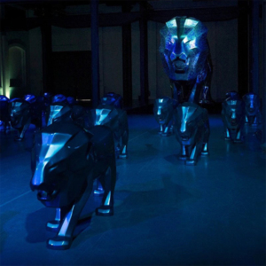 Metal lion sculptures illuminated with blue light, set in a dark room.