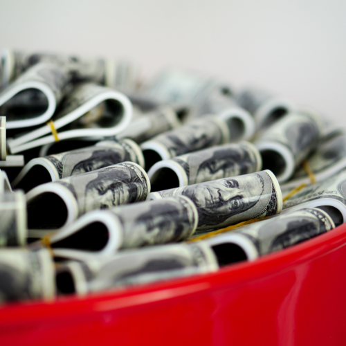 Czarna metalowa beczka z logo Audi i stosami zwiniętych banknotów dolarowych wystającymi z góry.