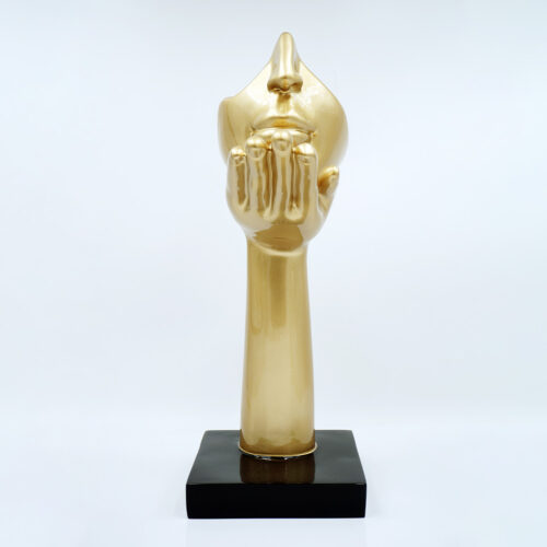 Złota rzeźba przedstawiająca dłoń wzniesioną do ust twarzy o zamkniętych oczach, na czarnej podstawie, na białym tle.