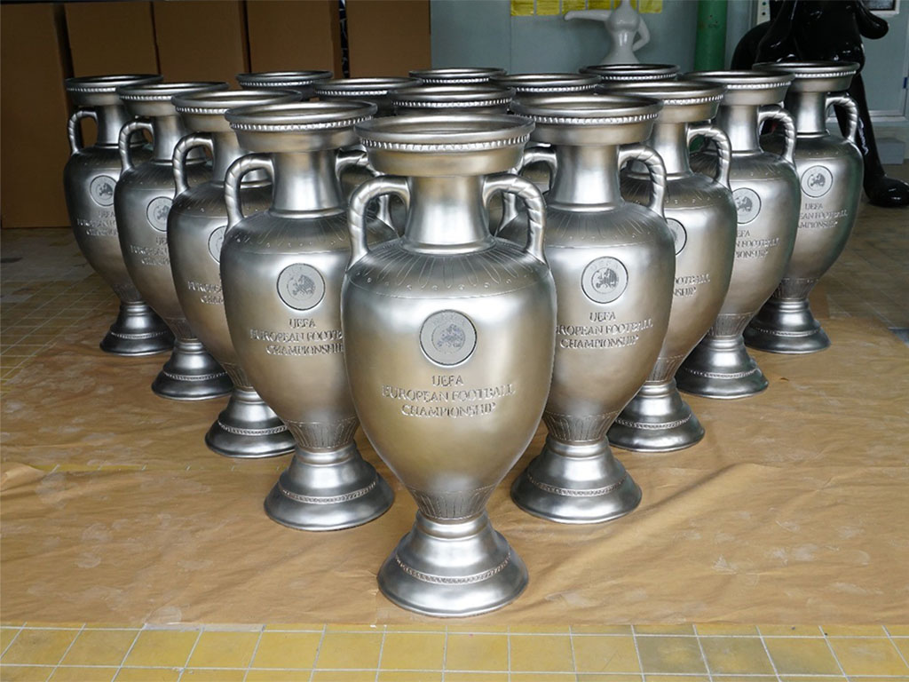 oryg_064490685_1129949550544944_1465385417682452480_o Kilka srebrnych trofeów UEFA European Football Championship ustawionych w dwóch rzędach na podłodze wewnątrz pomieszczenia.