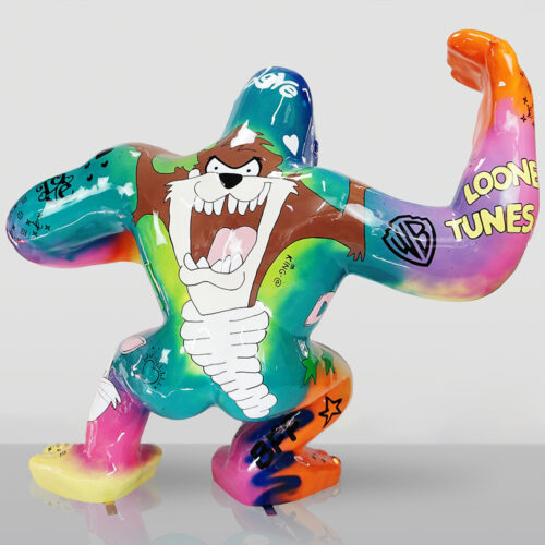 Kolorowa rzeźba przedstawiająca postać Taz z Looney Tunes z uniesionym mięśniowym ramieniem, ozdobiona graffiti i napisami, stojąca na przezroczystej powierzchni na jasnym tle.