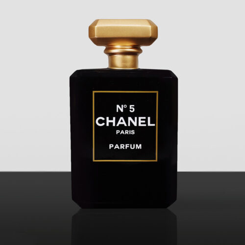 czarna butelka perfum Chanel No 5 z złotą nakrętką i białym napisem na przedzie stojąca na czarnej powierzchni na jasnoszarym tle