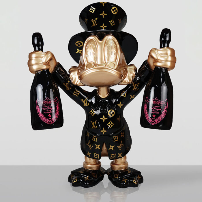 Złota i czarna figurka kaczora w cylindrze i płaszczu w monogramie Louis Vuitton trzymająca dwie butelki szampana Dom Pérignon Vintage 2009 z różowymi etykietami, na białym tle i odbiciem na powierzchni pod spodem.