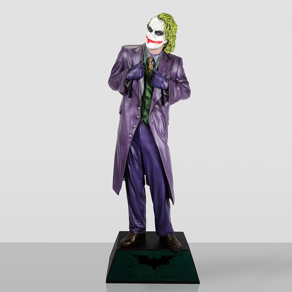Figura Dekoracyjna - Joker 3 Figurka Jokera z filmu "The Dark Knight" w fioletowym płaszczu, zielonej kamizelce i fioletowych spodniach stojąca na czarnym podwyższeniu z logo Batmana i napisem "The Dark Knight".