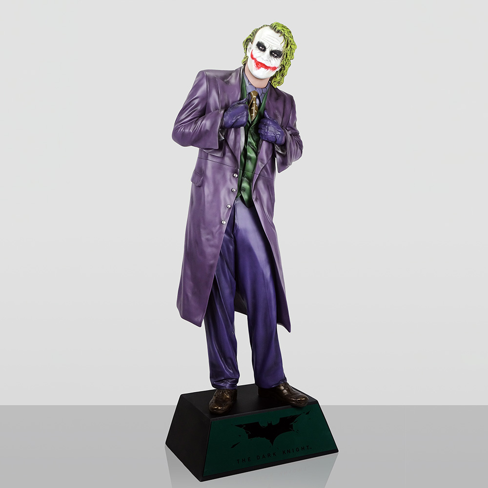 Figura Dekoracyjna - Joker 1 Figurka Jokera z filmu The Dark Knight, ubrana w fioletowy płaszcz, zieloną kamizelkę i spodnie, stojąca na czarnej podstawce z logo Batmana i napisem The Dark Knight