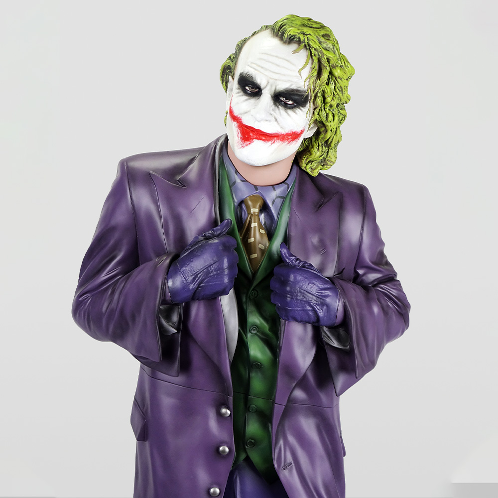 Figura Dekoracyjna - Joker 2 Postać w przebraniu Jokera z zielonymi włosami, białą twarzą z czerwonym uśmiechem i czarnymi oczami, ubrana w fioletowy garnitur, zieloną kamizelkę i fioletowe rękawiczki, na jasnym tle