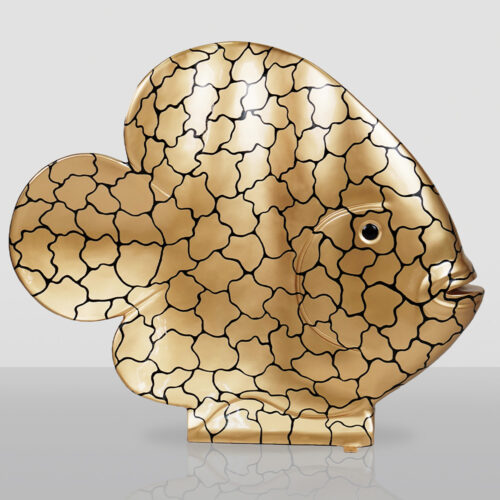 Ceramiczna figurka w kształcie ryby o złotej powierzchni z czarnym wzorem przypominającym nieregularne plamy, ustawiona na płaskiej powierzchni z odbiciem.