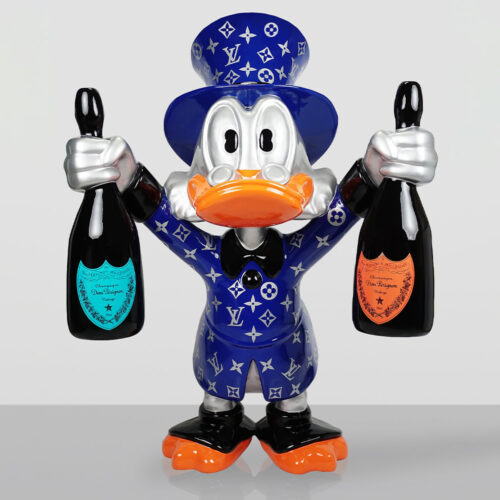 Ceramiczna figurka kaczora w niebieskim kapeluszu i płaszczu z logo Louis Vuitton, trzymająca w każdej ręce butelkę szampana Dom Pérignon, stojąca na szarej powierzchni z szarym tłem.