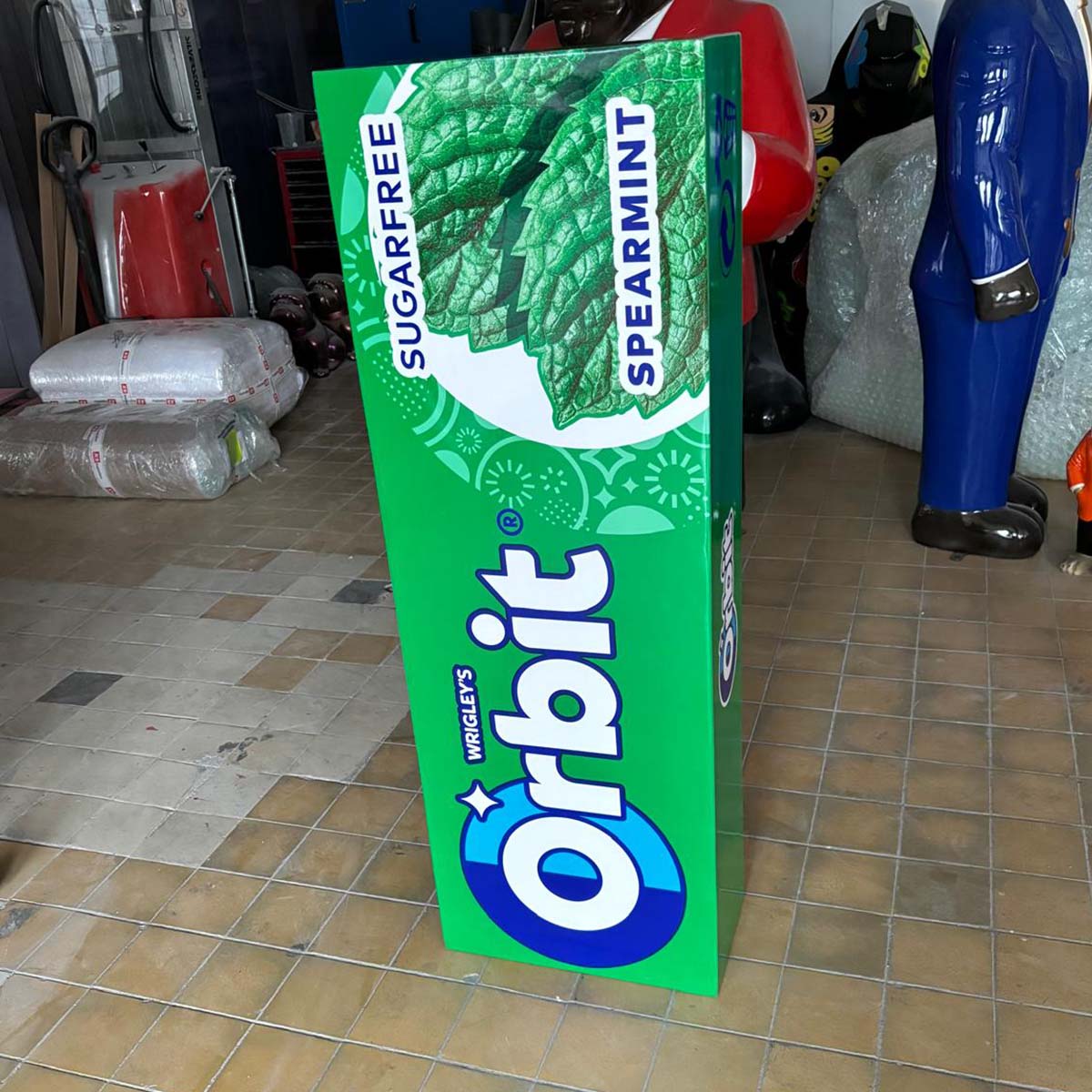 Wysoka figura reklamowa w kształcie batonika Orbit o zielonym opakowaniu, wykonana jako figura z laminatu.