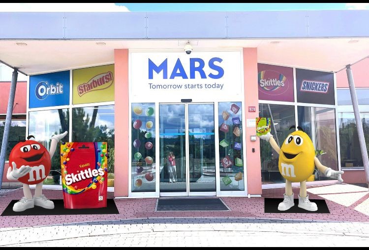 Przed wejściem do budynku stoją kolorowe figury z laminatu przedstawiające czerwone i żółte M&M'sy jako figura reklamowa.
