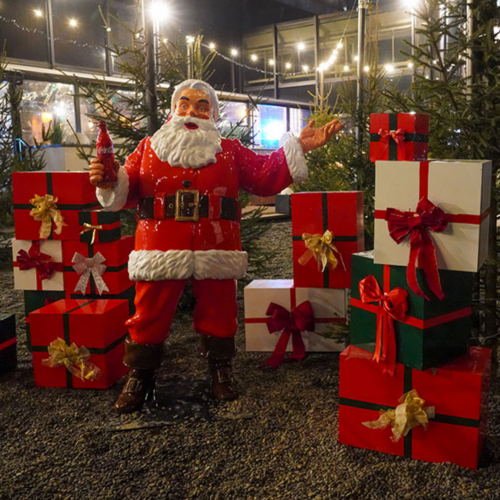 figura Świętego Mikołaja z laminatu w czerwonym stroju trzyma butelkę Coca‑Cola, dekoracyjna rzeźba świąteczna na outdoor/event
